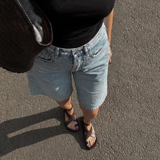 Woman wears A. Emery Jalen leather sandals, Arket long shorts, a black Loewe tank top and a Dragon Diffusion bag while walking. 