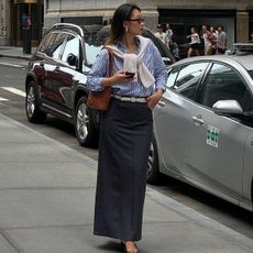 Caroline wears a striped button down shirt, beige sweater, brown bag, white belt, and black pencil skirt.