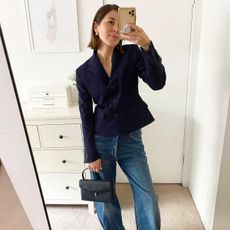 Judith wears wide-leg jeans, a navy blazer, and a black handbag.