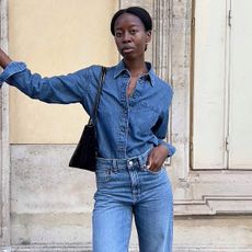 Influencer Sylvie Mus wearing a double denim outfit with a denim chambray shirt and denim straight leg French girl jeans, standing on a street in Paris.