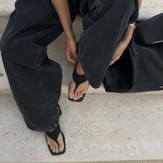 A woman wears black wide leg jeans and black flip-flops.