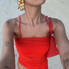 A woman wearing a red top, a red shoulder bag, and gold floral earrings.