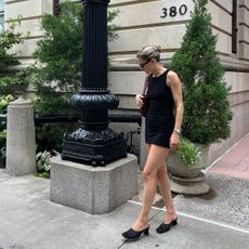 Eliza Huber wearing a black Norma Kamali minidress with black satin mules, sunglasses, and a burgundy Bottega Veneta shoulder bag. 